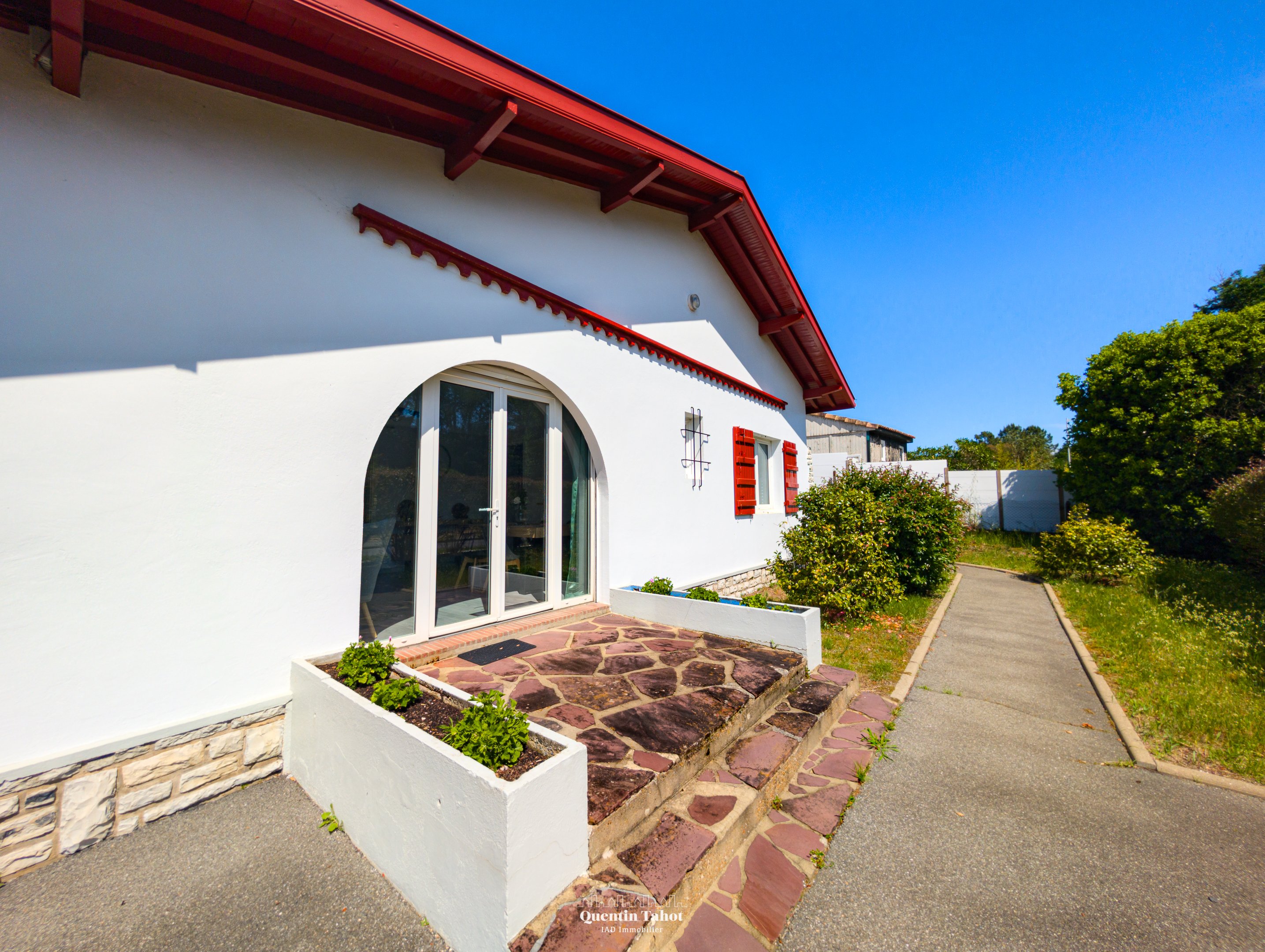 facade-villa-basque-volets-rouges-vendre-pays-basque-cote-landaise-quentin-tahot-iad.jpg alt="Façade d'une villa de style basque avec volets rouges et jardin arboré à vendre sur la Côte Landaise et le Pays Basque – Quentin Tahot IAD France"